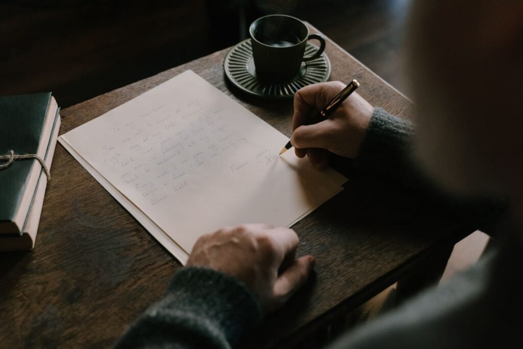 An adult writing a letter on a wooden desk with a cup of coffee