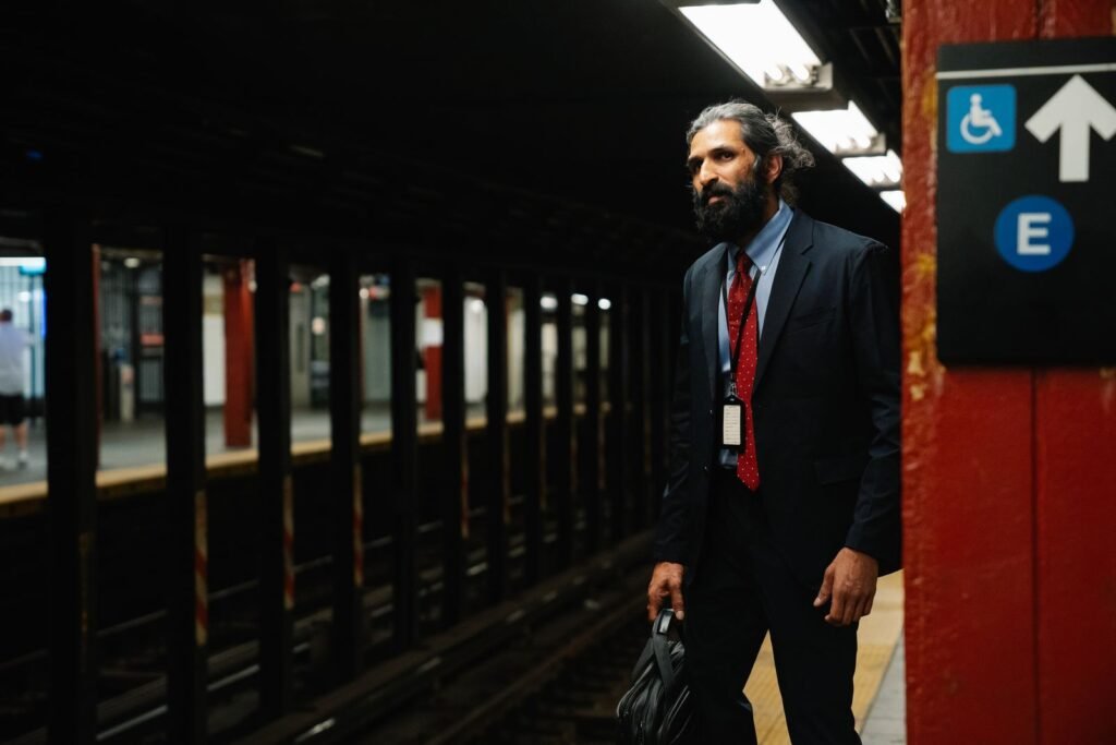 Bearded man in formal attire waiting at a subway platform holding a briefcase