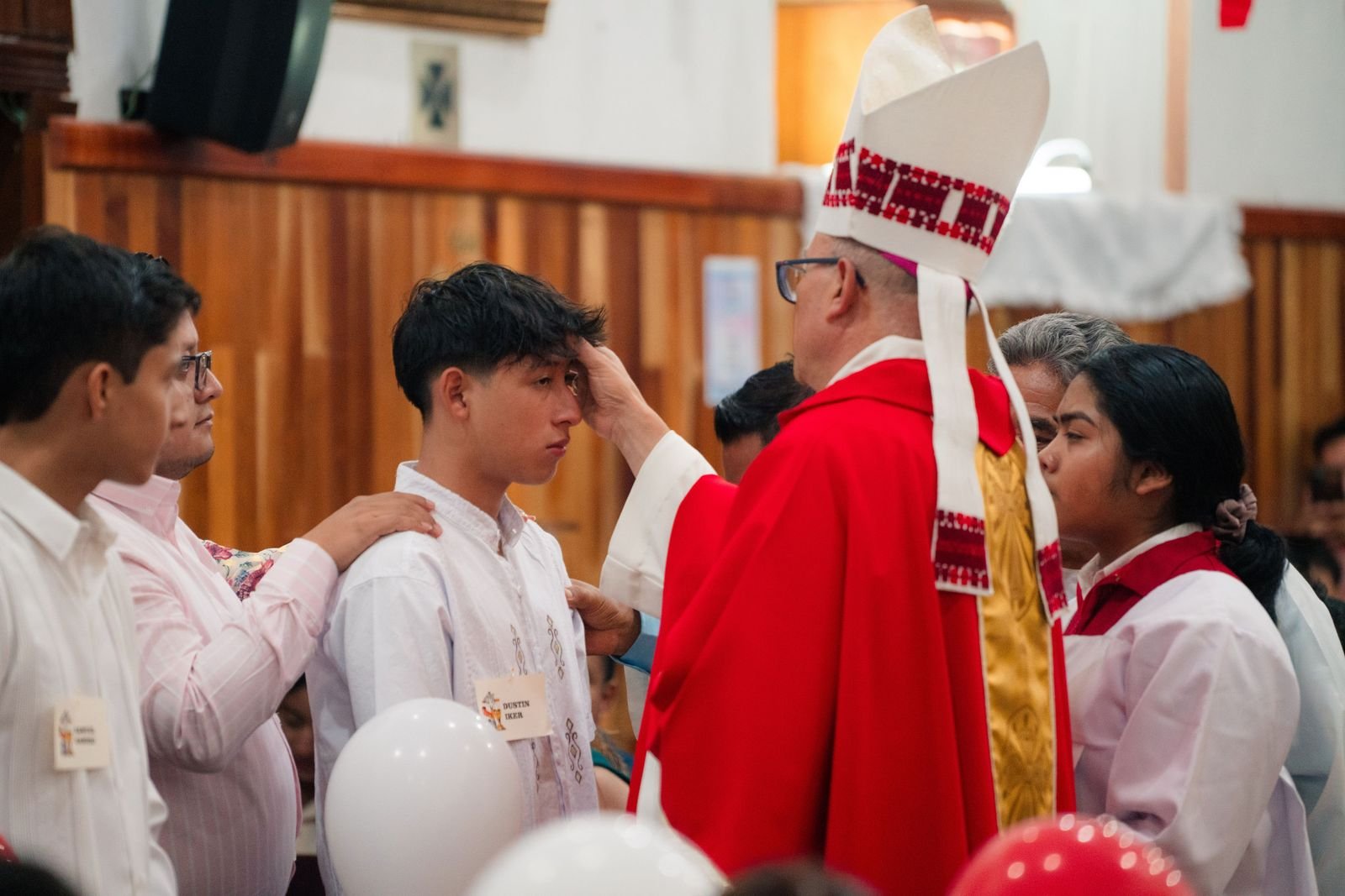 A bishop performs a confirmation ceremony, blessing a young man in a church setting