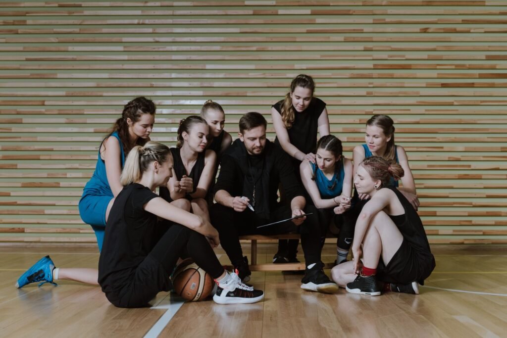 A coach strategizes with a women's basketball team in a gymnasium