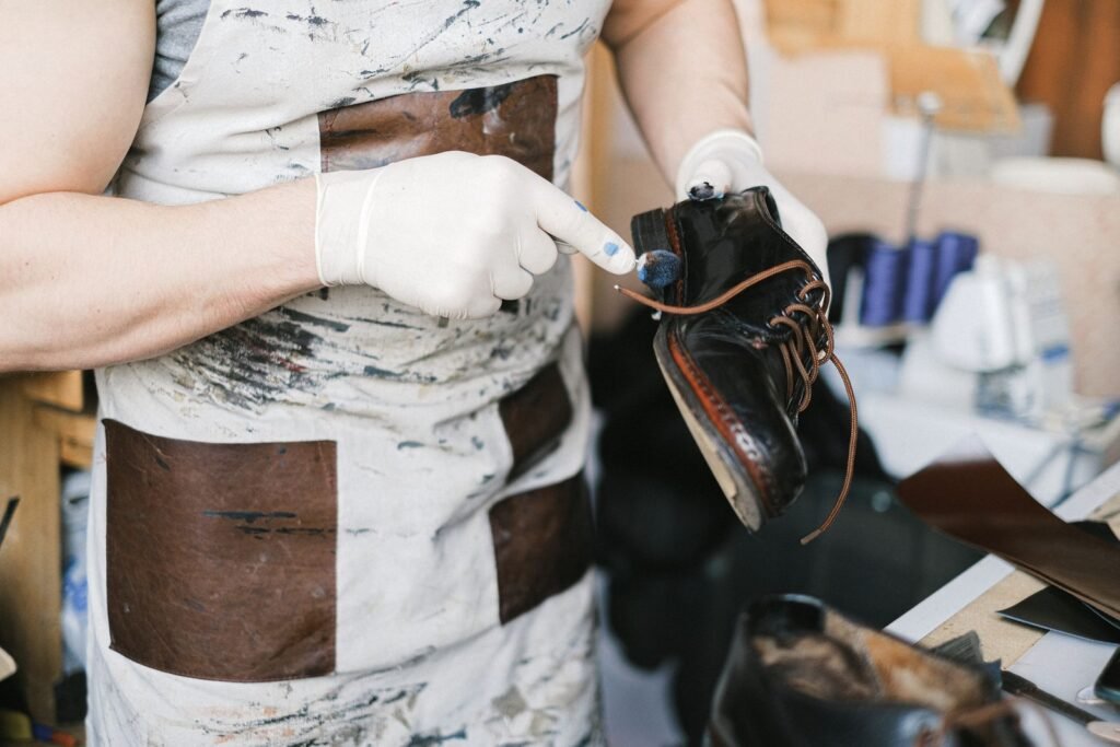 A craftsman polishing black leather shoes with gloves in a workshop