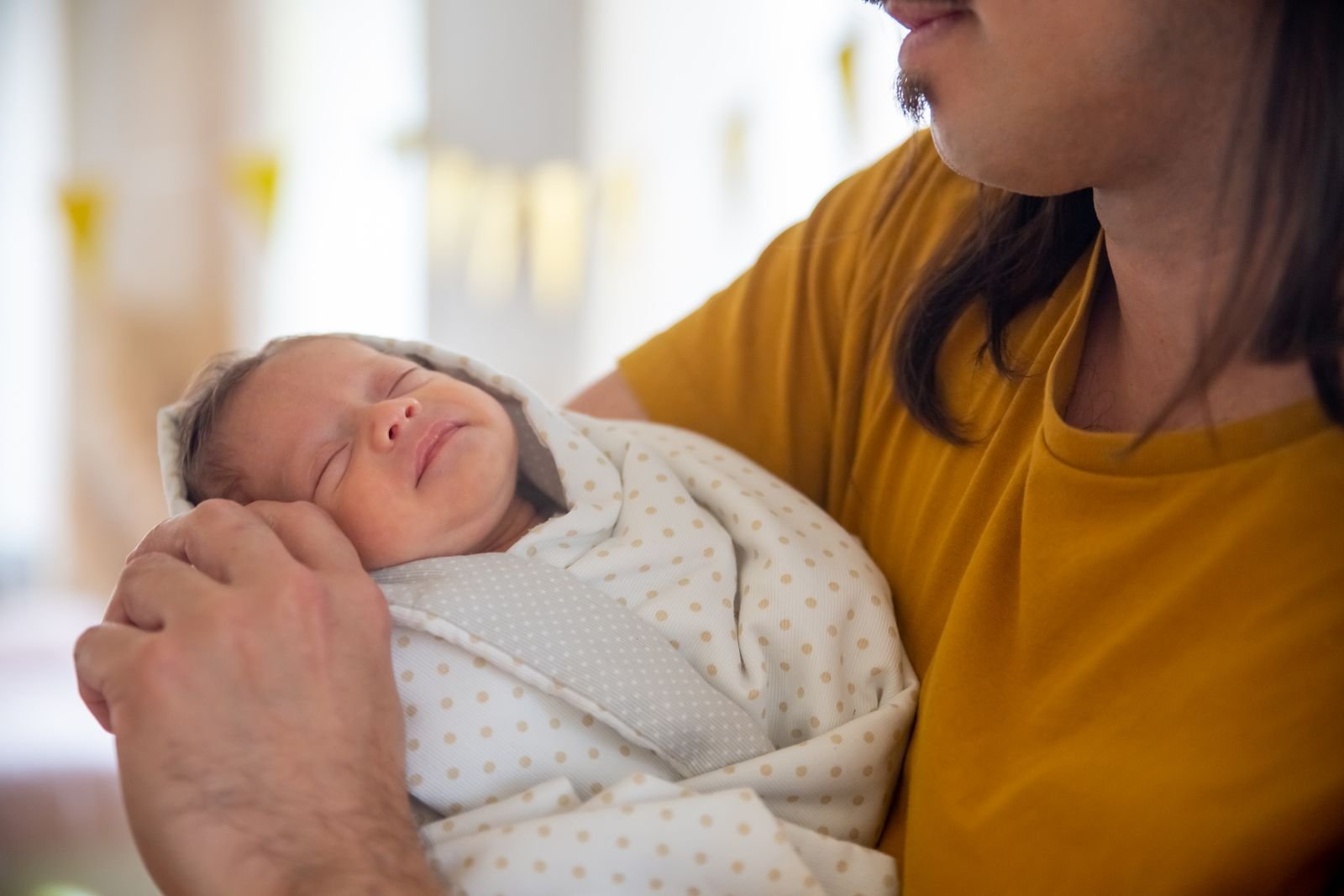 A father tenderly holding his sleeping newborn baby indoors