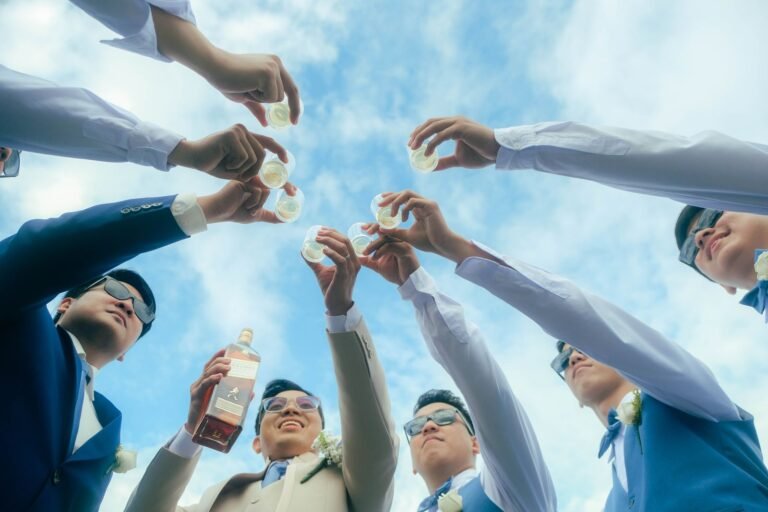 A group of groomsmen raising a toast under a clear blue sky