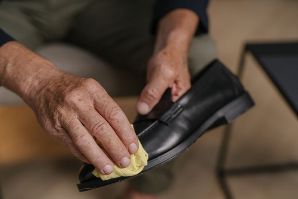 Detailed image of hands polishing a black leather shoe with a yellow cloth