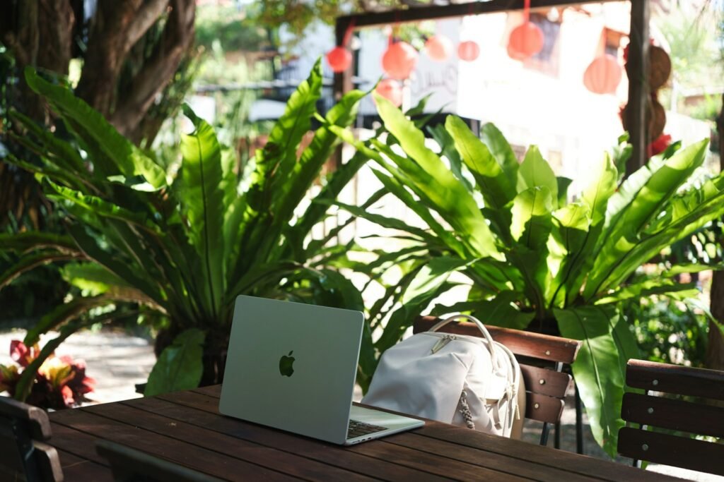 Laptop and backpack resting on a wooden table surrounded by plants
