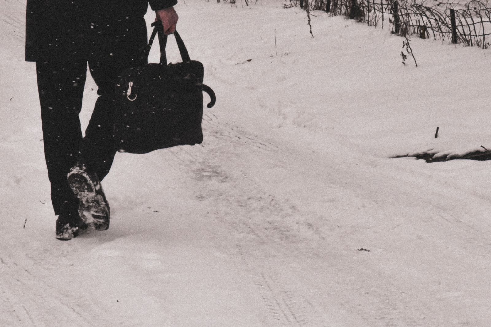 Adult walking through a snowy winter landscape holding a leather bag