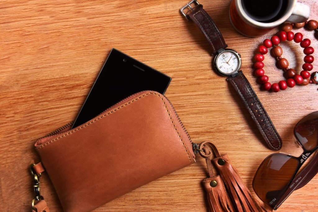 Flat lay of a leather wallet, wristwatch, sunglasses, and coffee on a wooden surface
