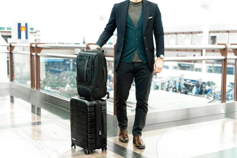 Man in a blue suit jacket standing beside a black travel bag