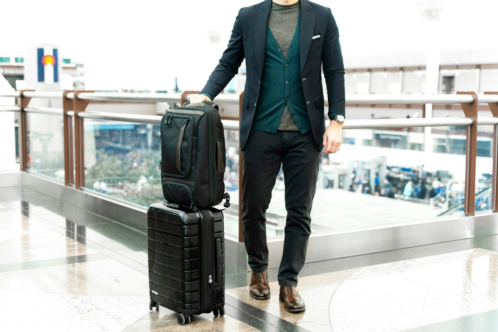 Man in a blue suit jacket standing beside a black travel bag