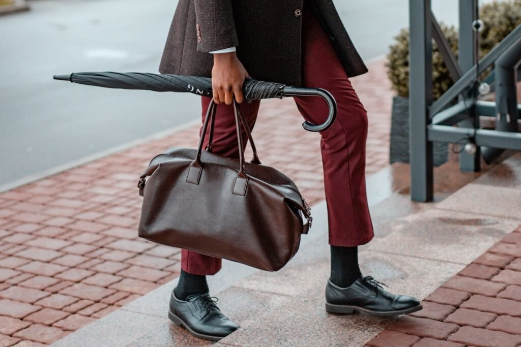 Man dressed in formal wear walking with a leather bag and umbrella on a rainy day