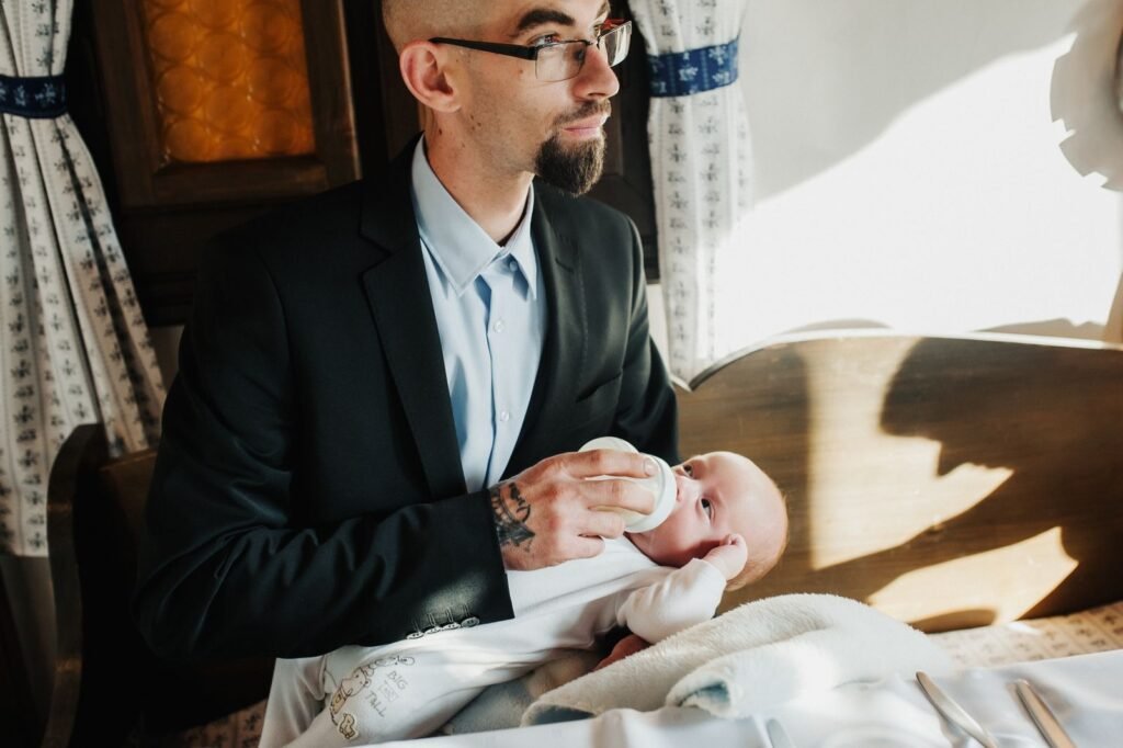 Man in a suit feeding a baby with a bottle in a cozy indoor setting