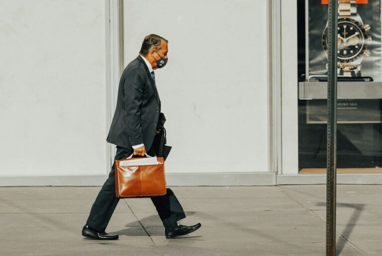 Man in a black suit jacket holding a brown leather briefcase