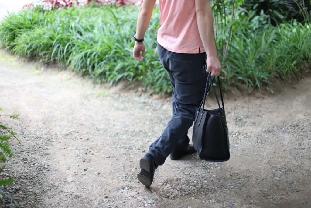 Stylish man in casual attire walking on a garden path carrying a bag