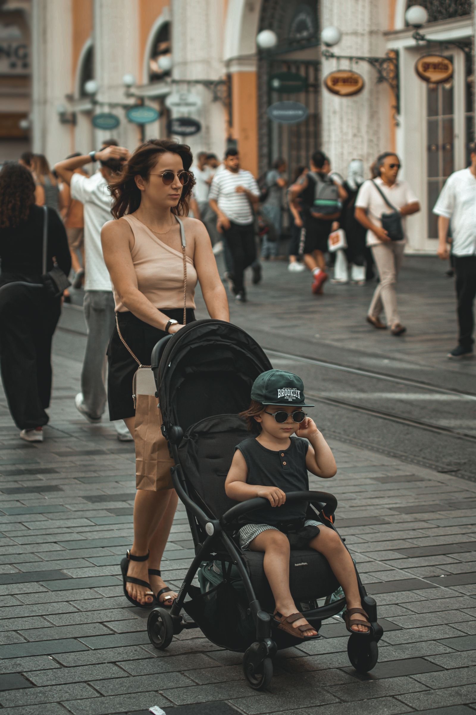 A mother pushes a baby stroller through a busy city street