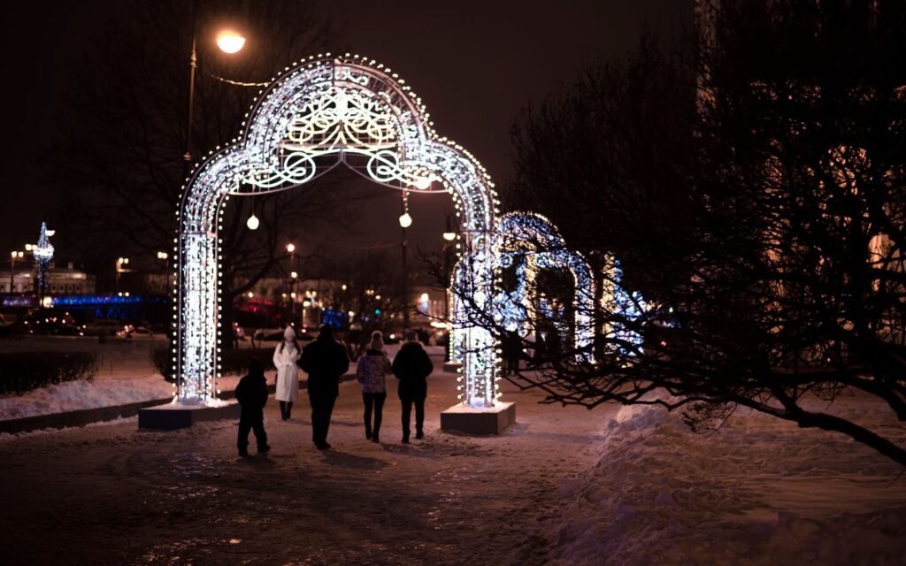 People walking under illuminated arches during a snowy winter evening