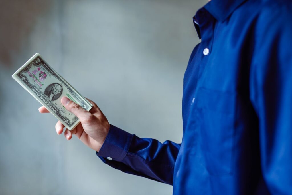 Person in a blue shirt holding a stack of US dollar bills