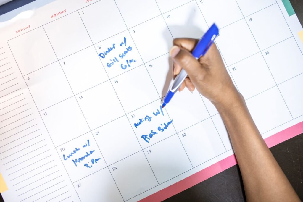 Person writing appointments on a calendar with a blue pen