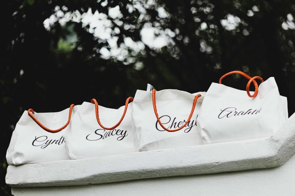 Four personalized tote bags with names and orange handles on display outdoors
