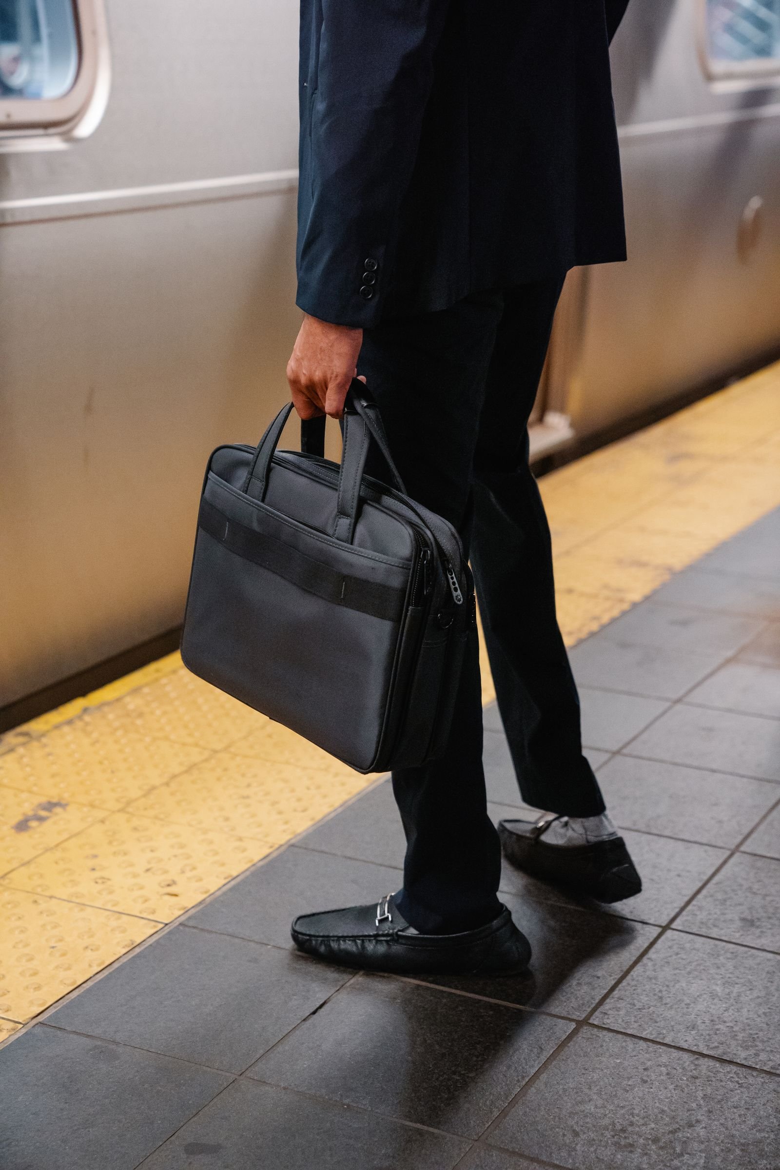 Professional in a suit holds a briefcase while waiting on a subway platform