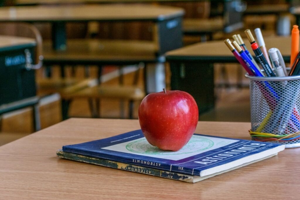 Red apple resting on books with stationery in a classroom