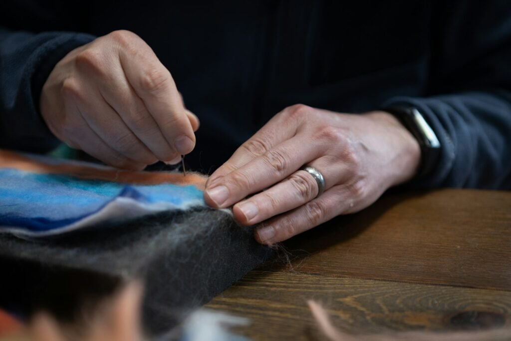 Hands sewing fabric with a needle and thread, representing hand labor