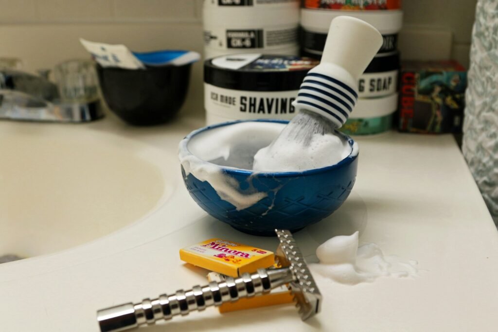 Shaving brush and bowl with lather and a razor on the sink