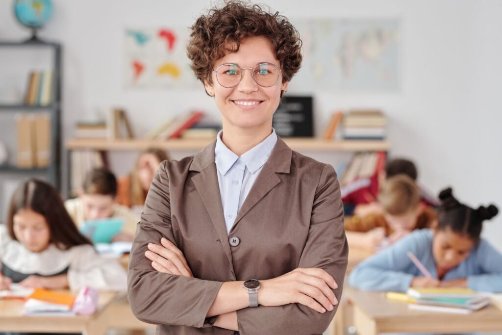 Smiling teacher with glasses standing with arms crossed in a classroom