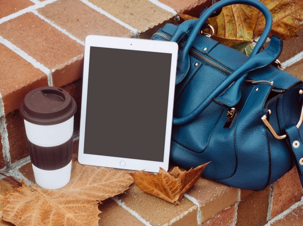 Tablet, coffee cup, and bag arranged in an autumn still life scene