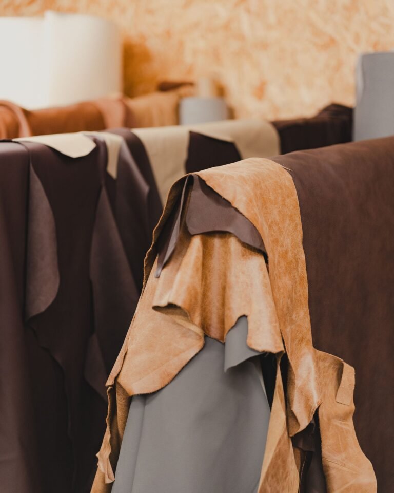 A collection of various tanned leather hides hanging indoors, showcasing different textures and colors