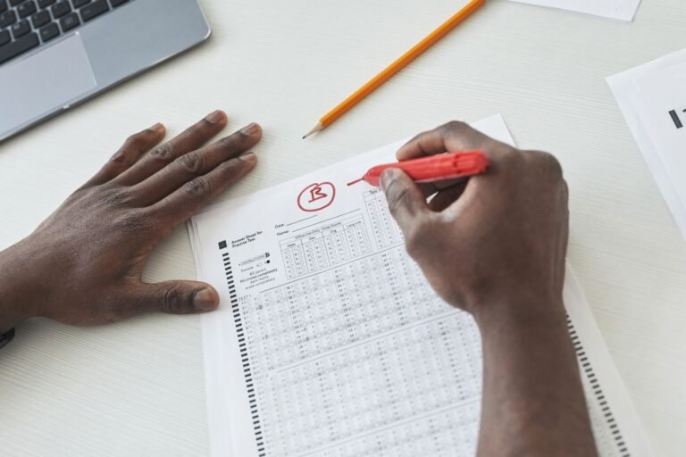 Close-up of a teacher grading multiple choice exams with a red pen