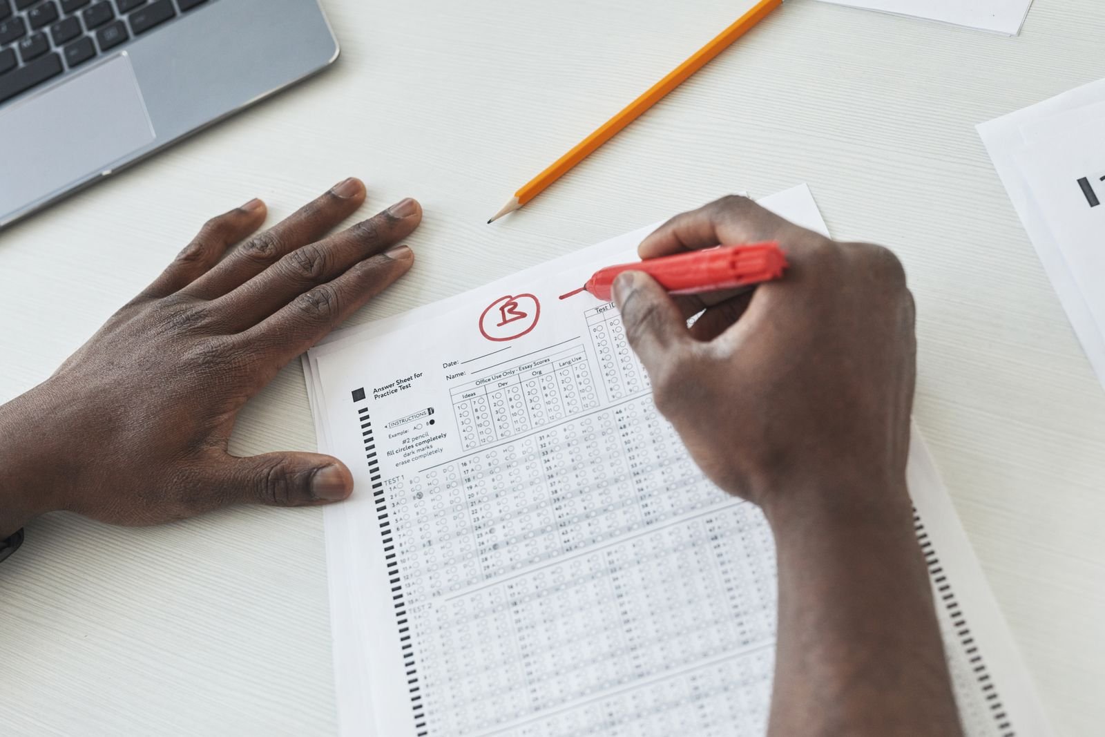 Close-up of a teacher grading multiple choice exams with a red pen