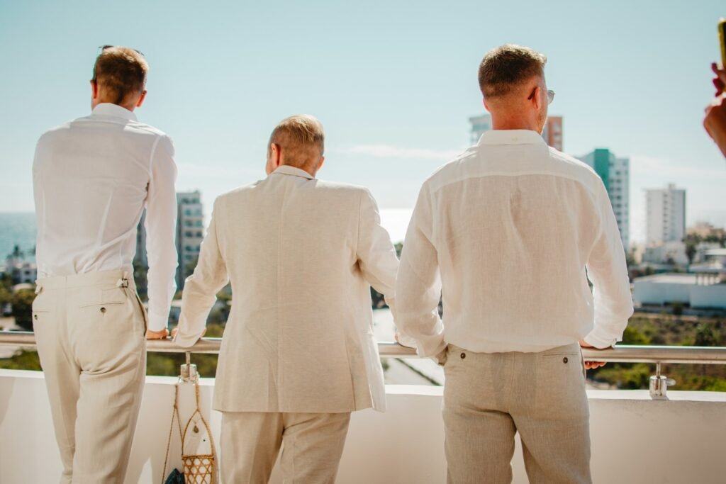 Three men in white suits standing on a balcony overlooking the city