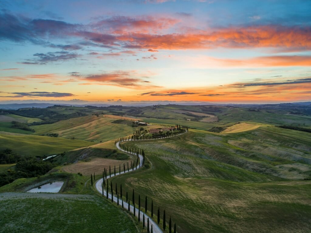 Road between a green grass field near mountains in Tuscany