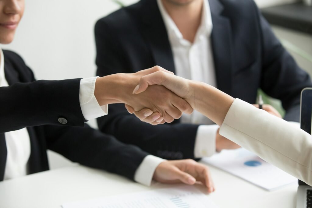 Two people shaking hands in front of a laptop during a client meeting