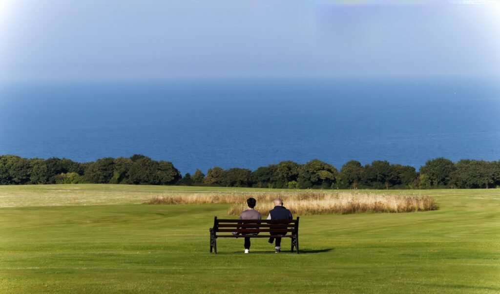 Two people sitting together on a bench in an open field, enjoying quiet retirement time