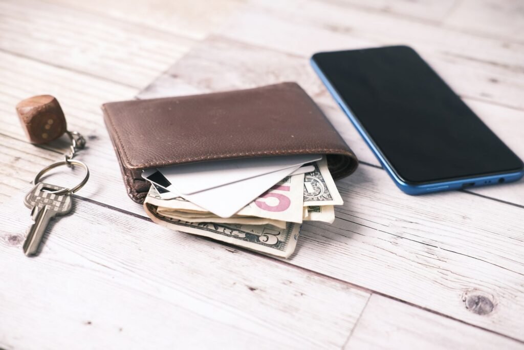 Close-up of a wallet with cash, smartphone, and keys on a wooden table