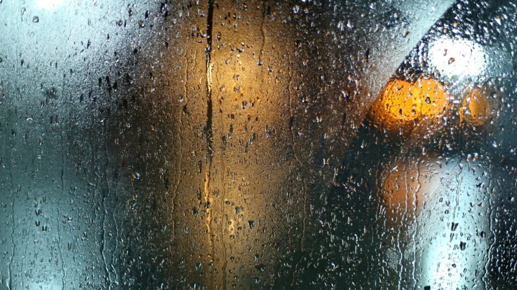 Wet window with rain droplets and a traffic light visible outside