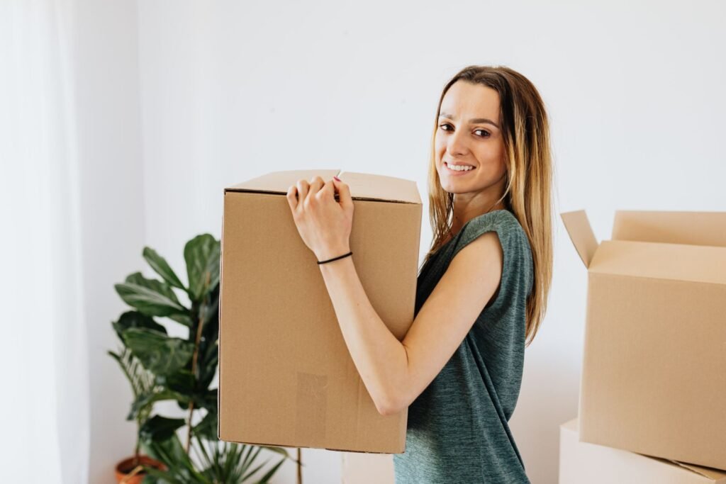 Smiling woman in casual clothes carrying a cardboard moving box