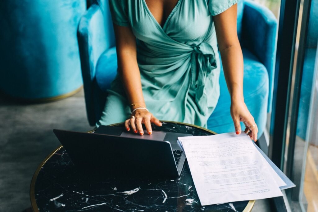 Adult woman in a teal dress working on a laptop with documents
