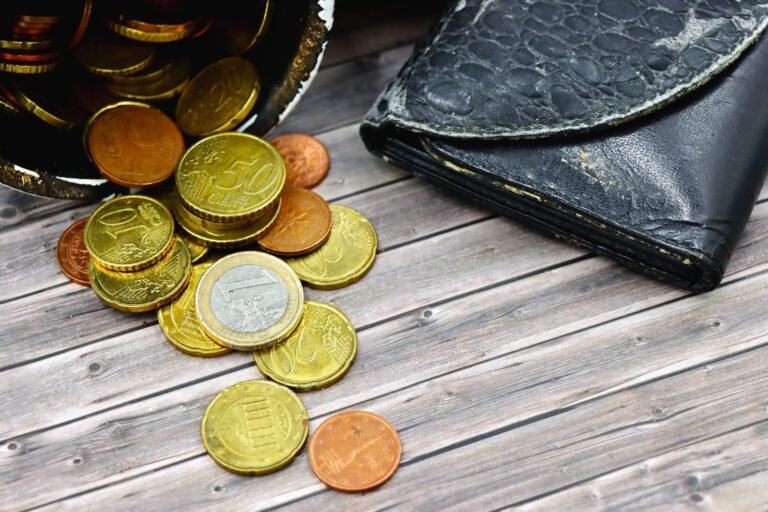 A worn-out leather wallet and scattered euro coins on a wooden surface